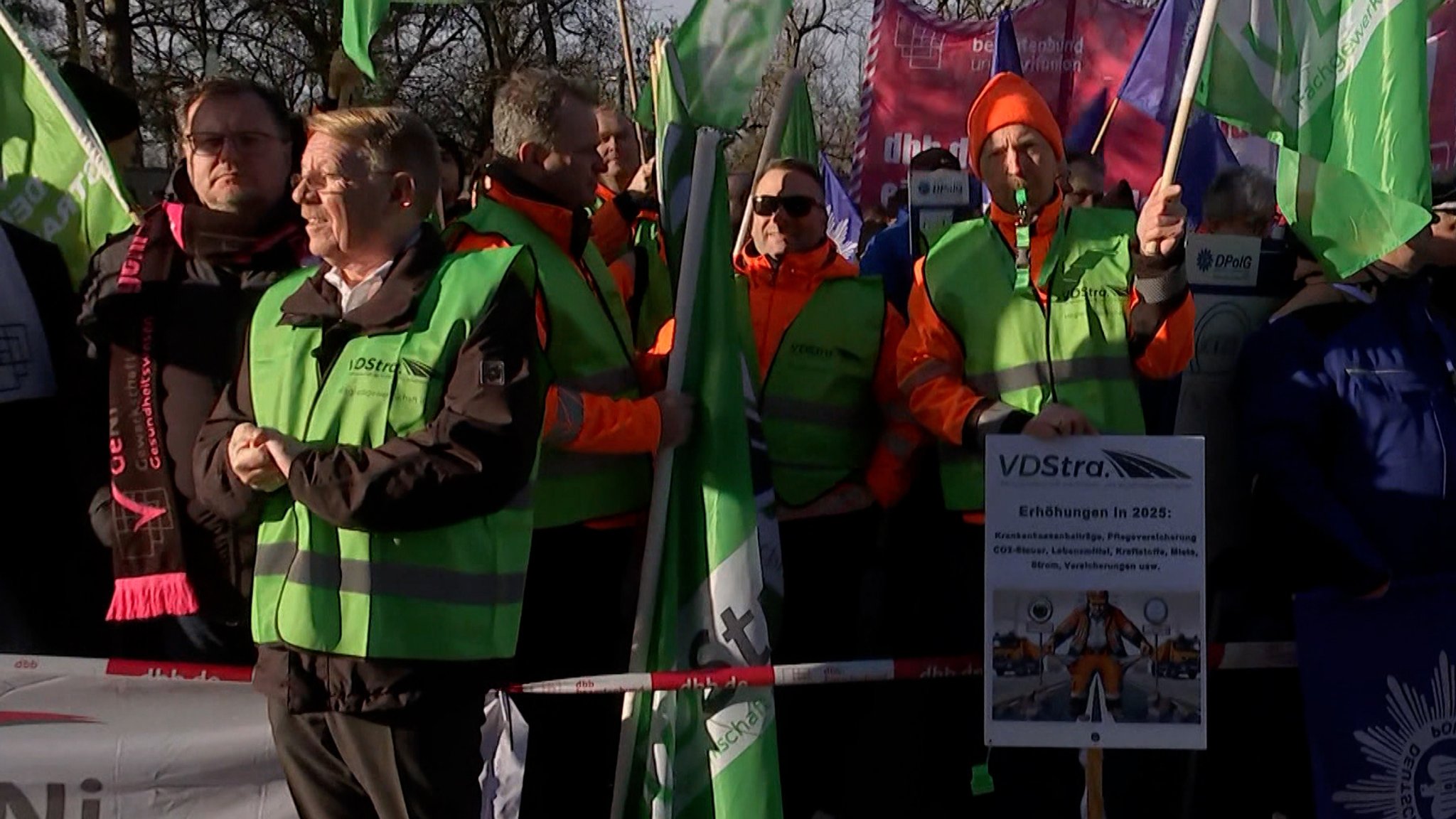 Streikende tragen Warnwesten, halten Fahnen und Plakate hoch. 