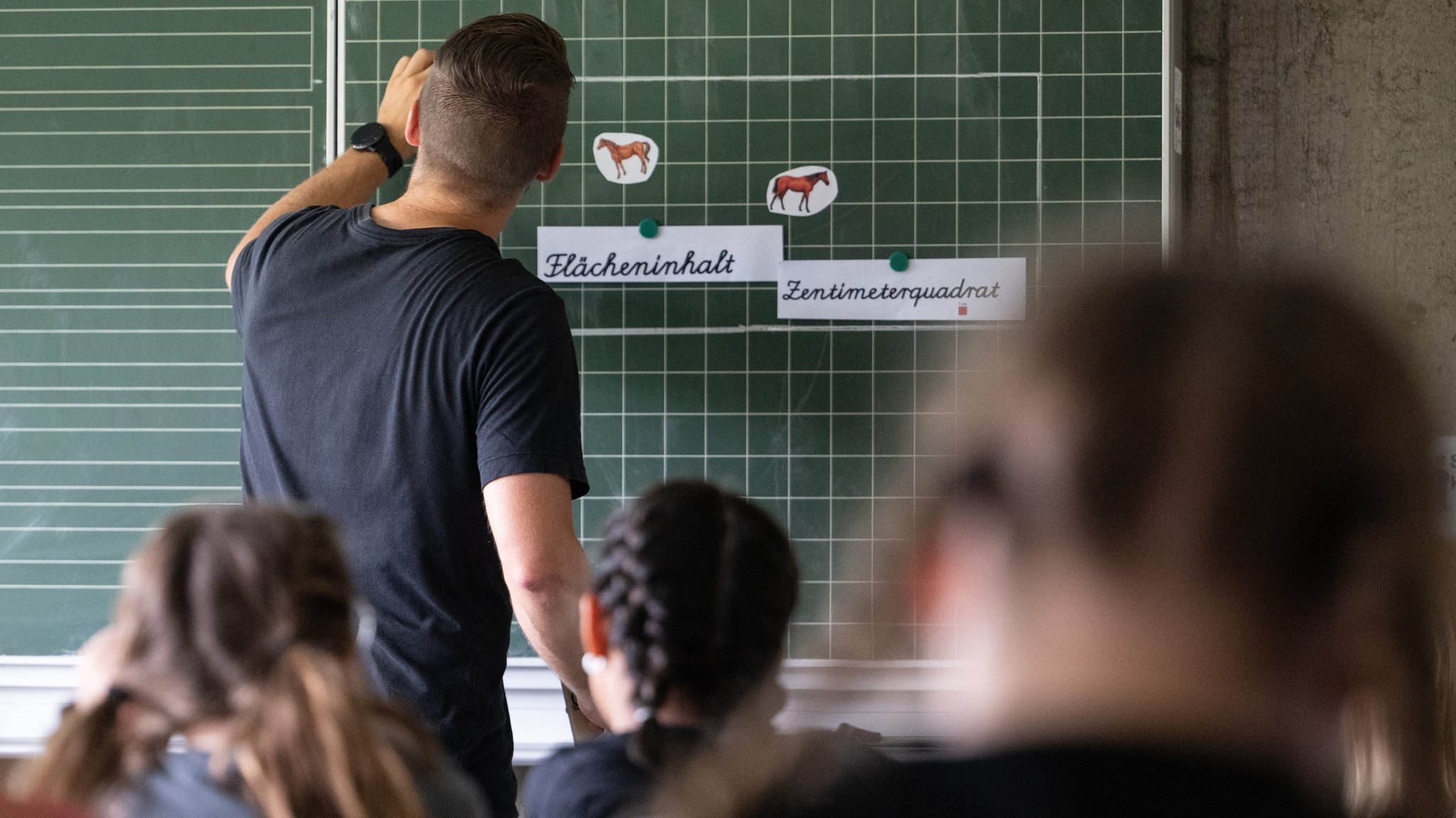 PRODUKTION - 27.06.2024, Baden-Württemberg, Neckartailfingen: Ein Lehrer macht im Unterricht einer vierten Klasse einer Grundschule einen Tafelanschrieb, während an der Tafel Zettel mit der Aufschrift «Flächeninhalt» und «Zentimeterquadrat» hängen. (zu dpa: «Hamburg vermeldet Rekord bei neu eingestellten Lehrkräften») Foto: Marijan Murat/dpa +++ dpa-Bildfunk +++