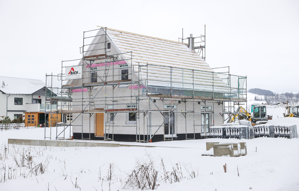 Der Rohbau eines Einfamilienhauses steht in einem verschneiten Baugebiet.
