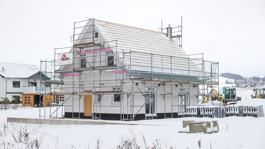 Der Rohbau eines Einfamilienhauses steht in einem verschneiten Baugebiet.