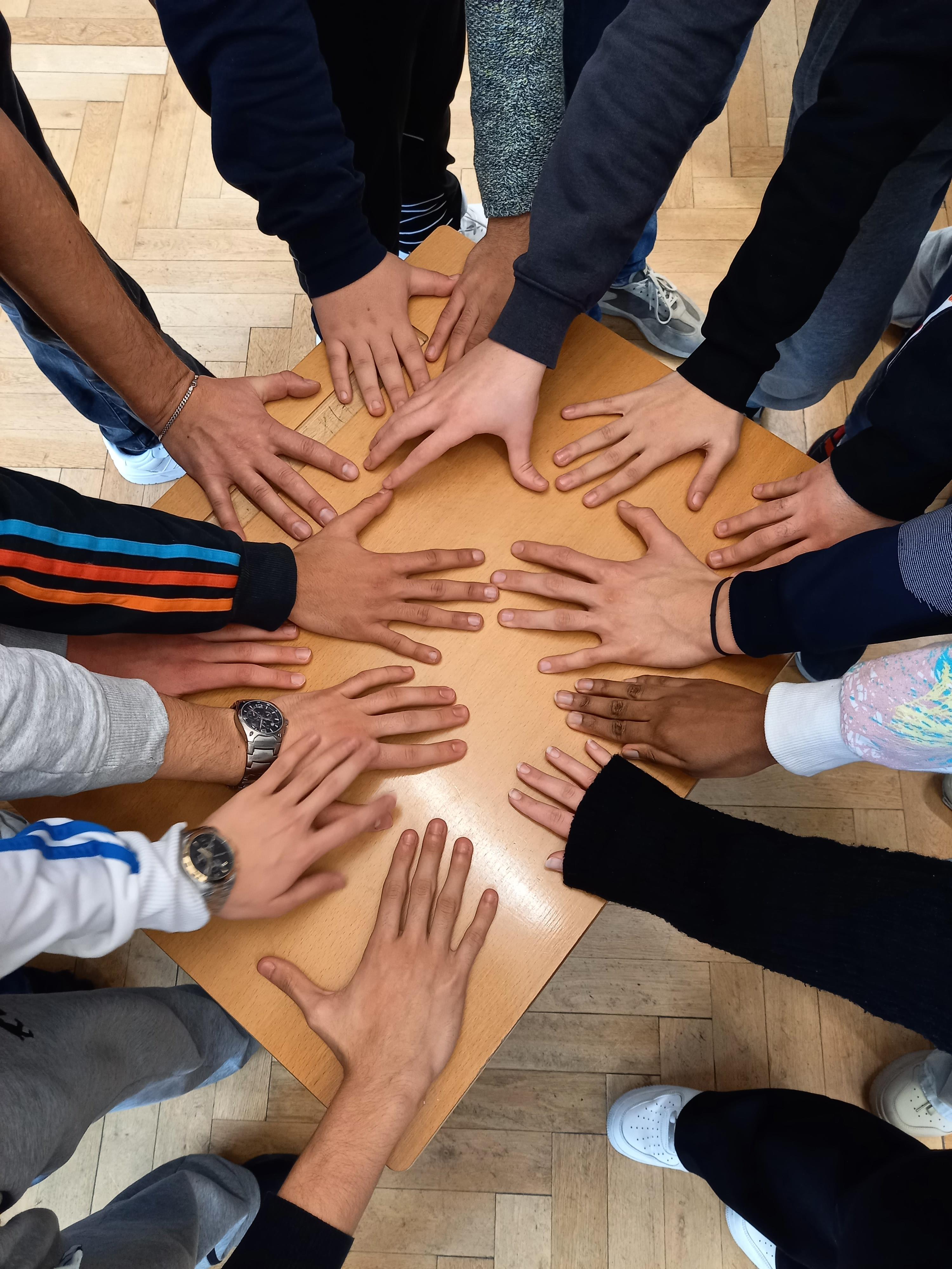 Schülerinnen und Schüler der 10a legen ihre Hände auf einen Tisch 