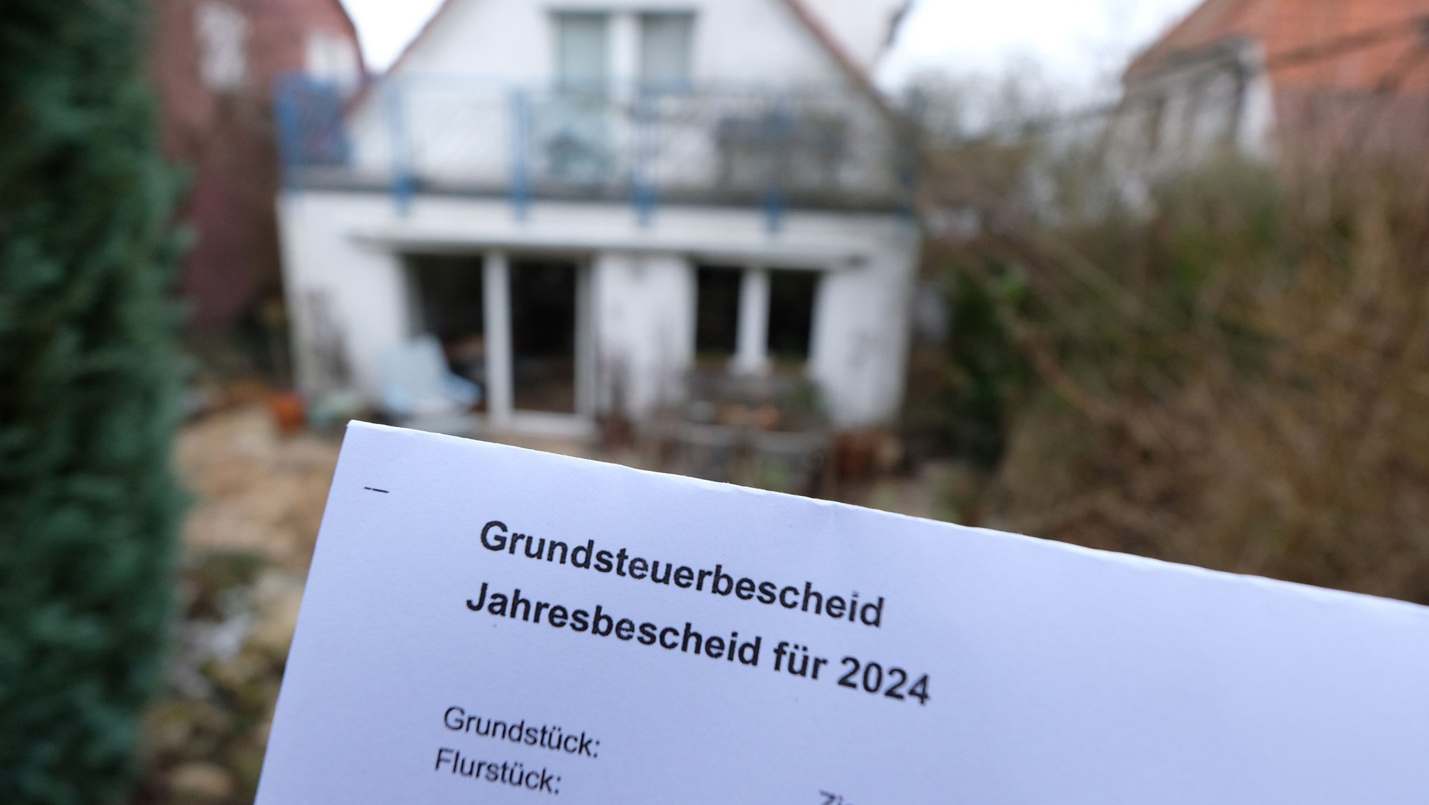 Ein Grundsteuerbescheid für 2024 wird vor einem Privatgrundstück gehalten