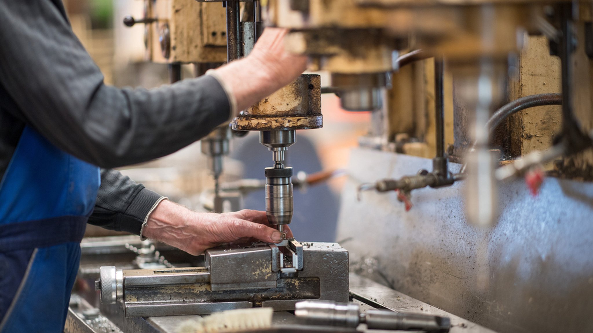 Ein Mitarbeiter bedient in der Produktionshalle eine Maschine zur Verarbeitung von Metall.