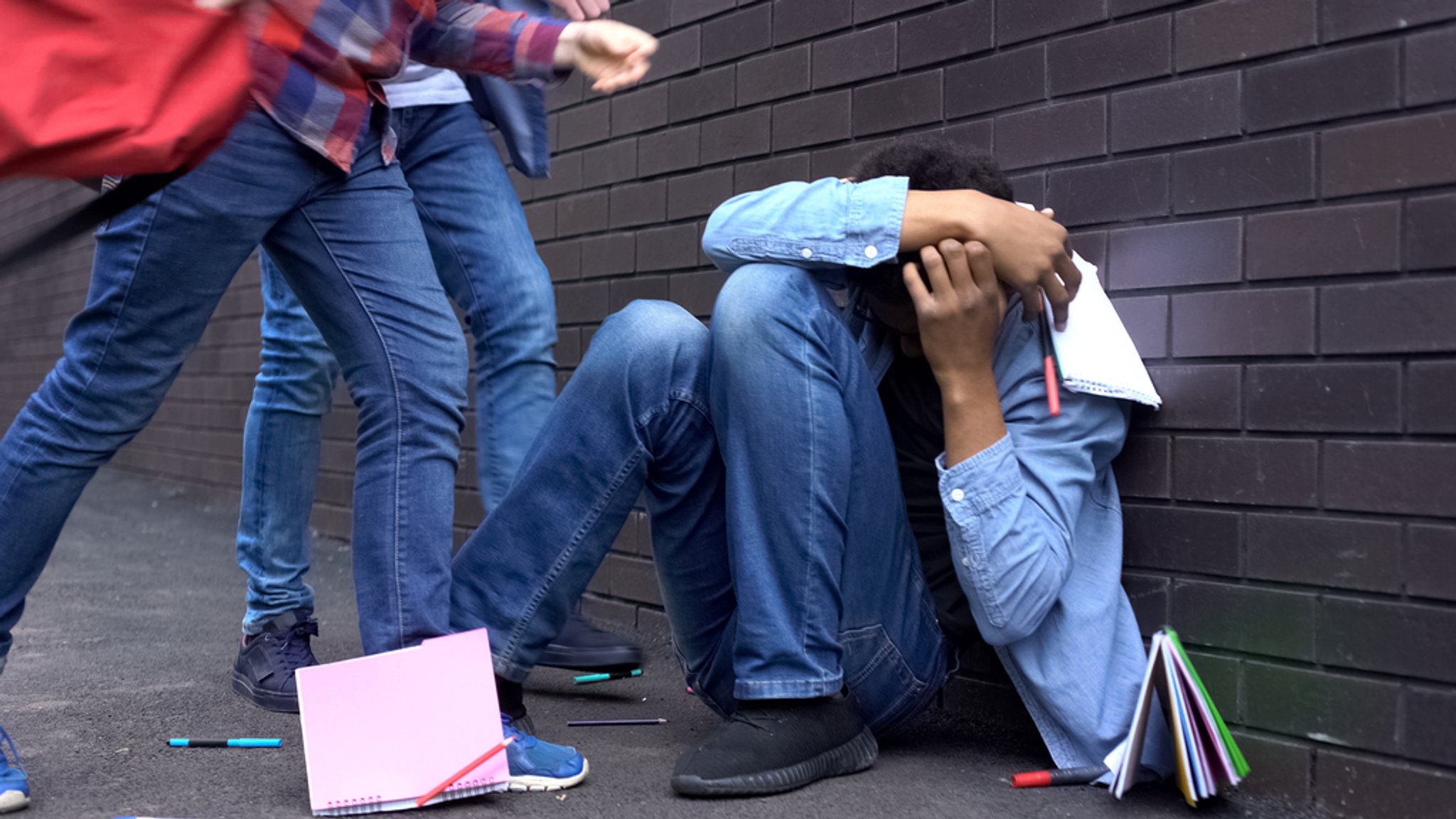 Symbolbild: Ein Junge wird an der Schule von seinen Mitschülern gemobbt und mit Schulbüchern beworfen.