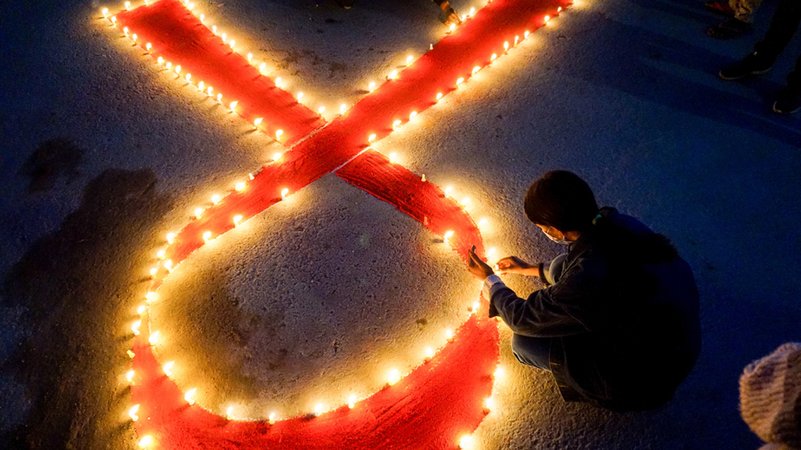Eine Frau stellt Kerzen auf, die eine rote Schleife formen - ein weltweit anerkanntes Symbol für die Solidarität mit HIV-Infizierten. | Bild: dpa-Bildfunk/Sunil Pradhan Eine Frau stellt Kerzen auf, die eine rote Schleife formen - ein weltweit anerkanntes Symbol für die Solidarität mit HIV-Infizierten.