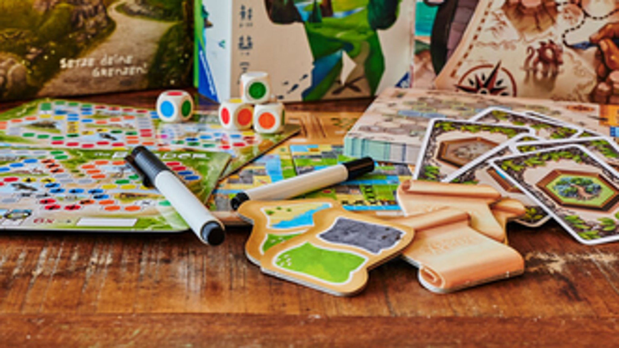 Ein Brettspiel mit farbigen Würfeln und Spielkarten liegt auf einem Tisch.