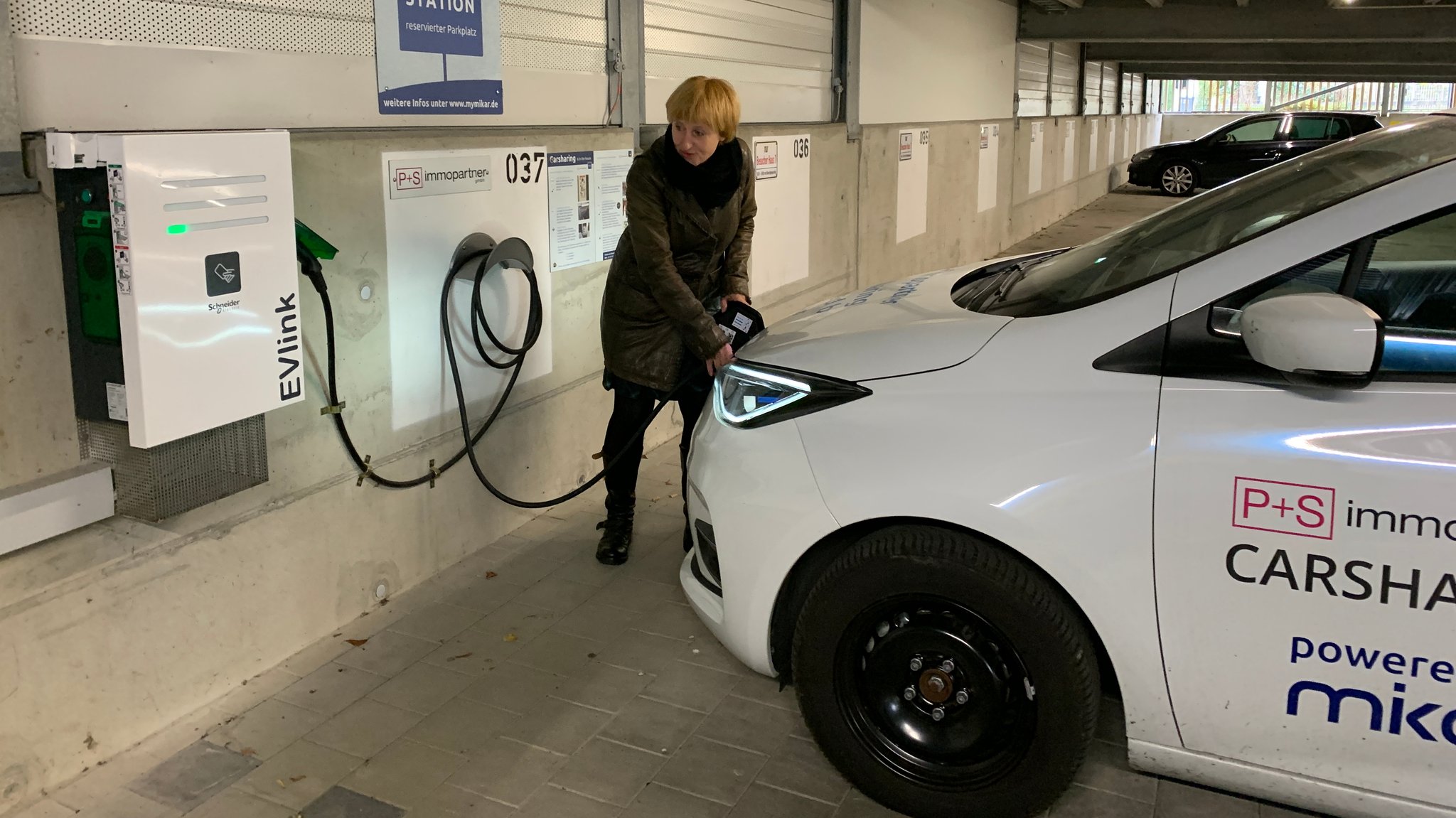 Eine Nutzerin steckt den Stecker am Elektroauto an, um es wieder aufzuladen. 