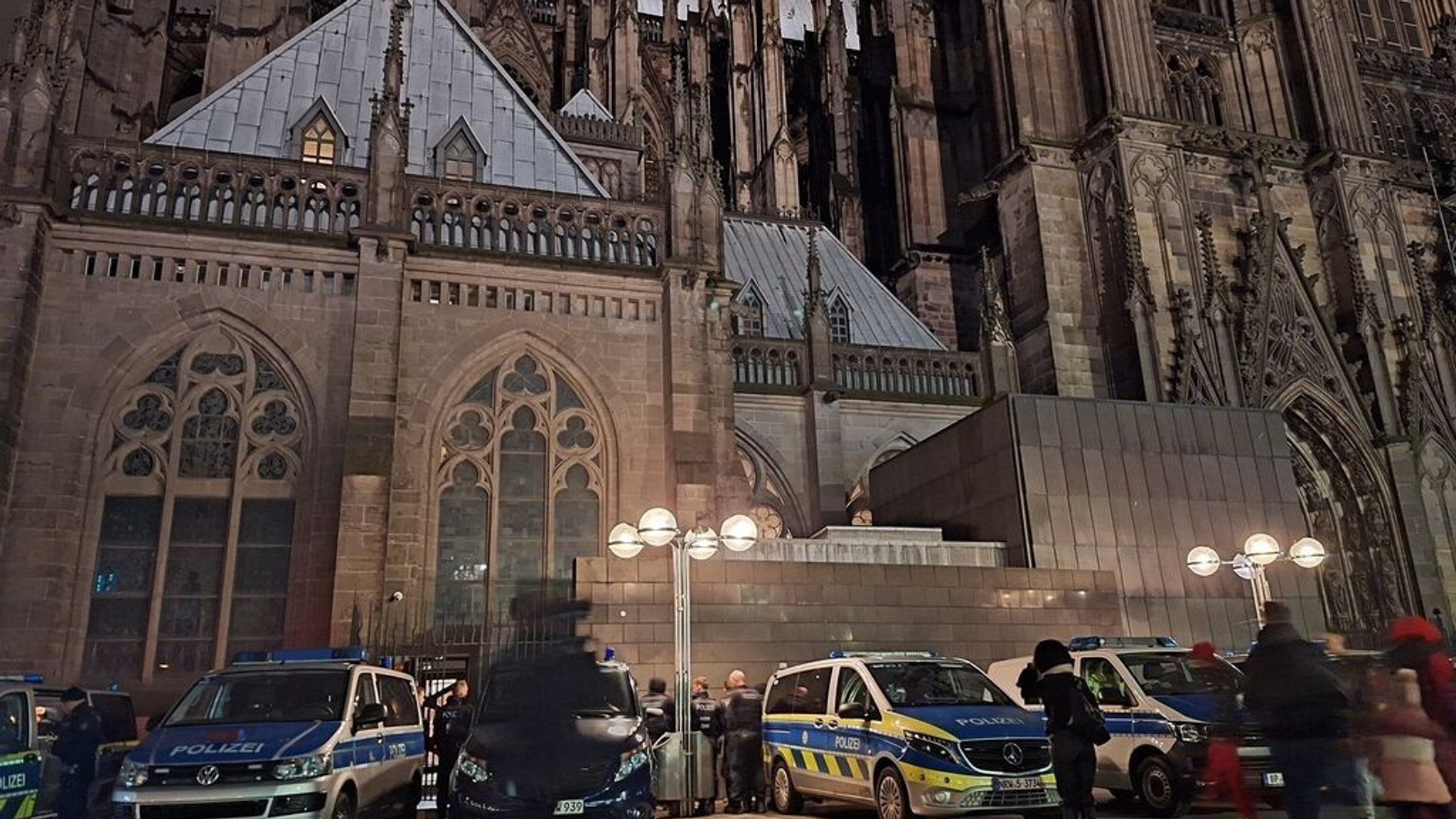 23.12.2023, Nordrhein-Westfalen, Köln: Einsatzfahrzeuge der Polizei stehen vor dem Dom. Gottesdienstbesucher des Kölner Doms und Touristen müssen sich in den nächsten Tagen auf erhöhte Sicherheitsstandards einstellen. Wegen eines Gefahrenhinweises werde die Polizei besondere Schutzmaßnahmen ergreifen, teilte die Behörde am 23.12.2023 mit. Der Staatsschutz, der bei politisch motivierten Straftaten aktiv wird, habe Ermittlungen aufgenommen. (zu dpa "Kölner Dom mit besonderen Schutzmaßnahmen: Spürhunde im Einsatz") Foto: Sascha Thelen/dpa +++ dpa-Bildfunk +++