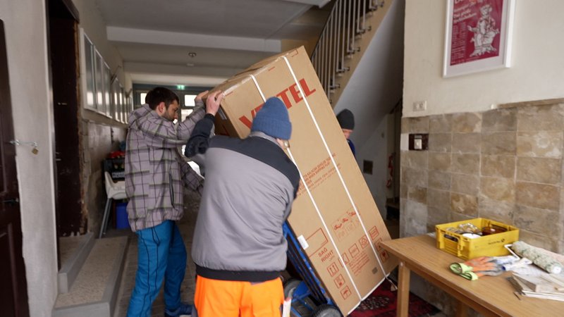 Zwei Männer tragen einen großen Karton durch einen Hausflur