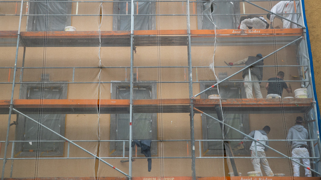 Arbeiter auf einem Baugerüst verrichten Arbeiten an der Fassade eines Hauses. 