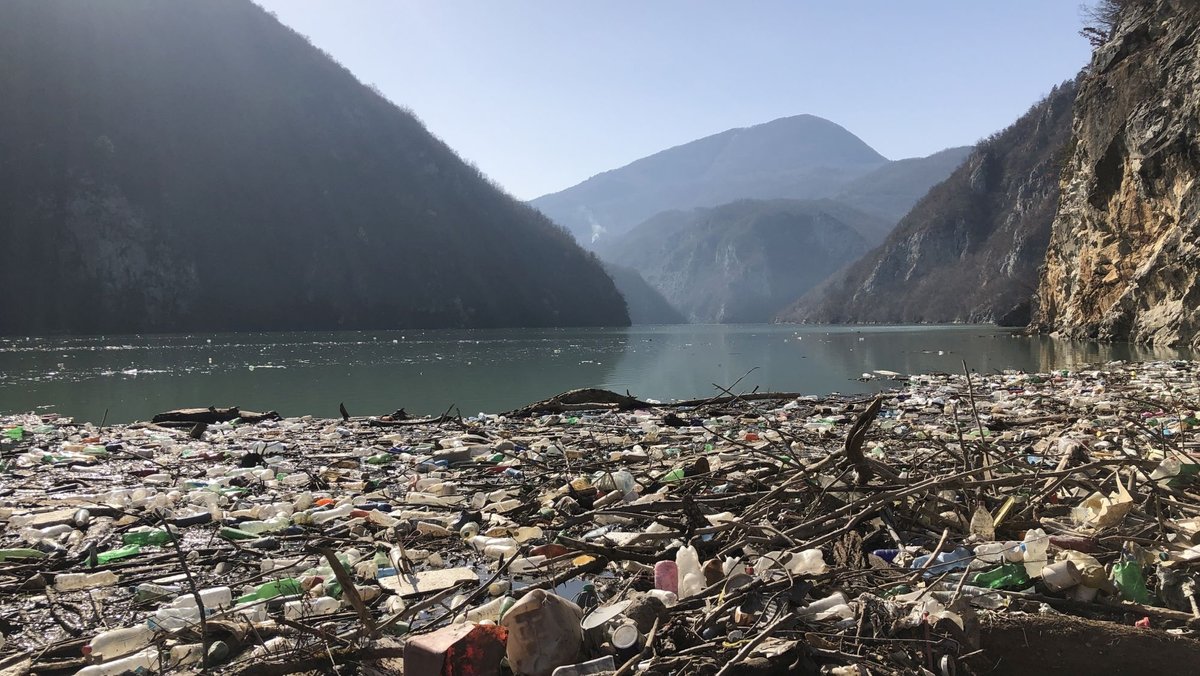 Das Bild zeigt einen Müllteppich auf dem Fluss Drina in Bosnien und Herzegowina. Im Hintergrund sind  die Berge zu sehen.