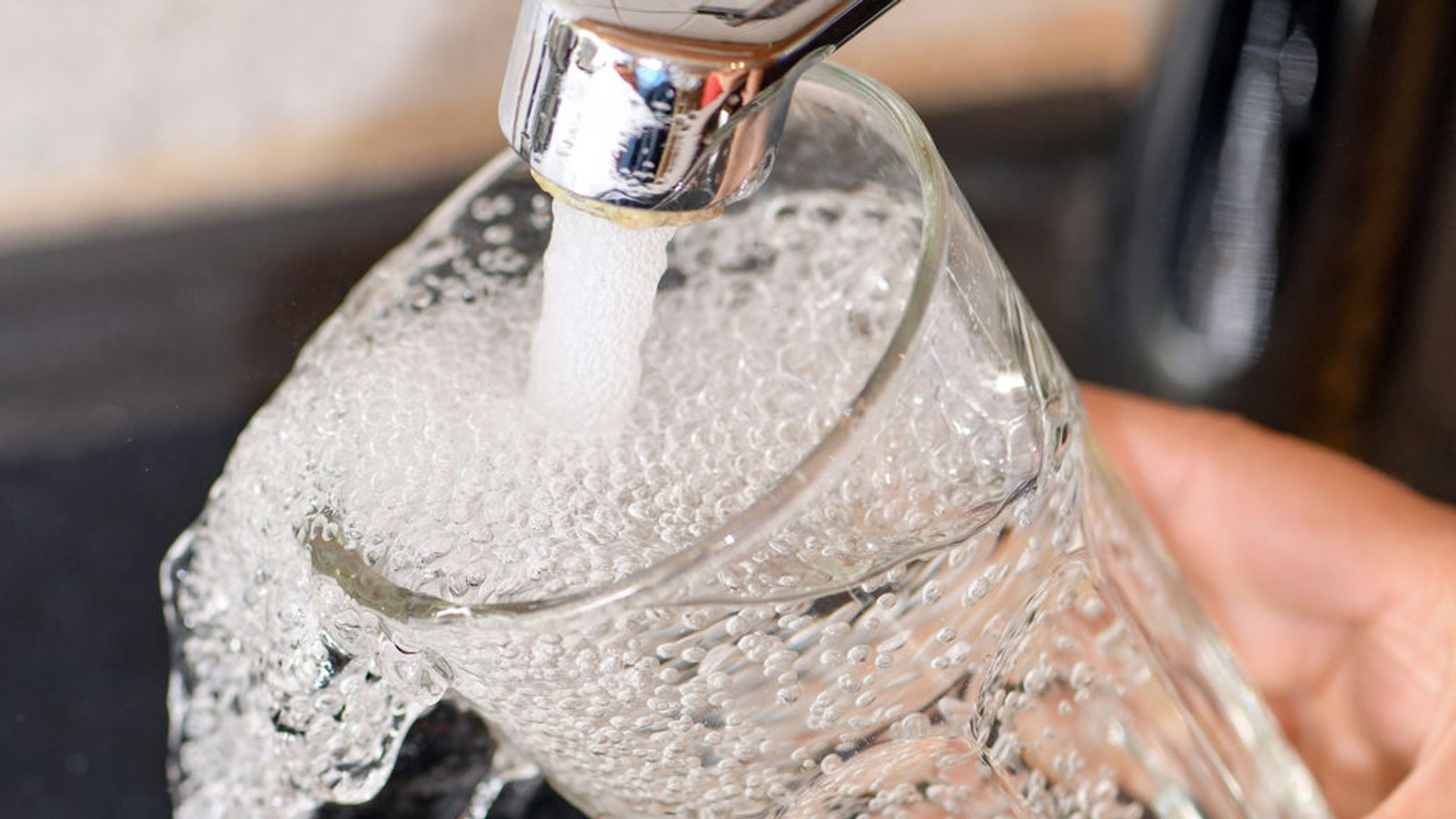 An einem Wasserhahn wird ein Trinkglas mit Leitungswasser befüllt (Symbolbild)