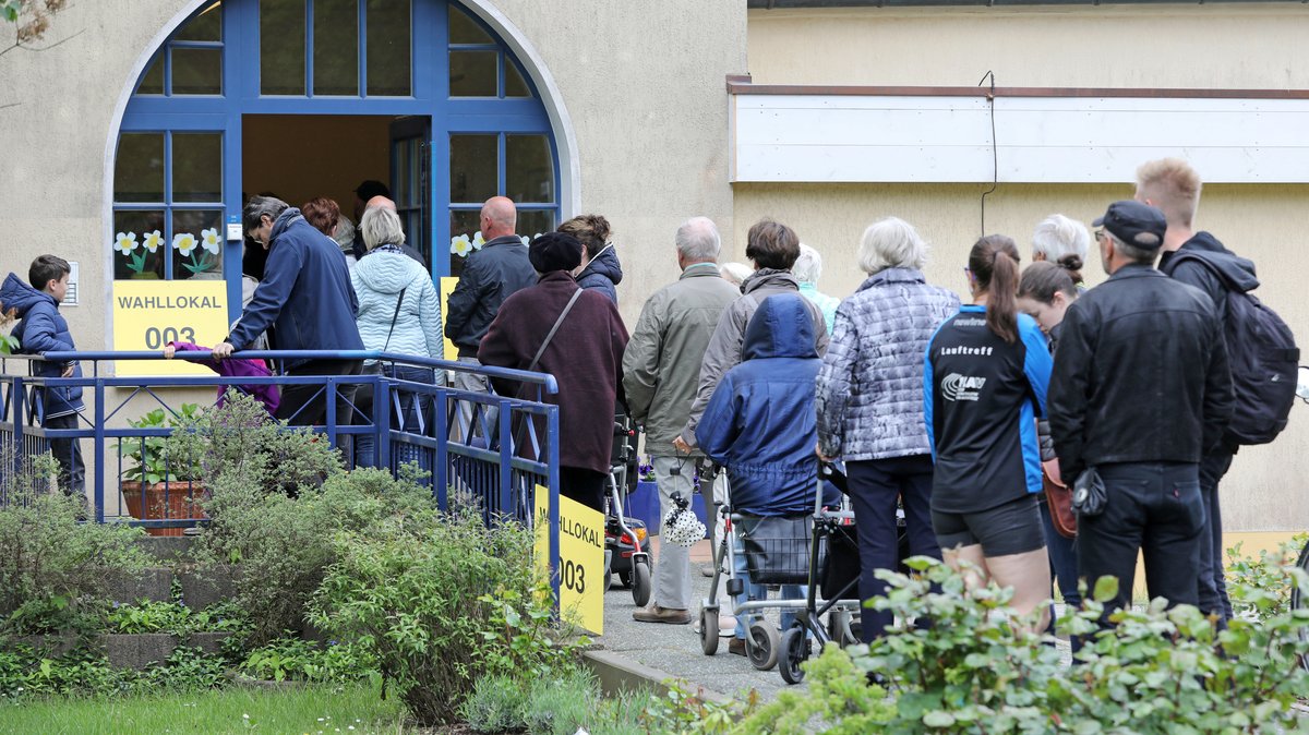 Eine Menschenschlange von hinten vor einem Wahllokal.