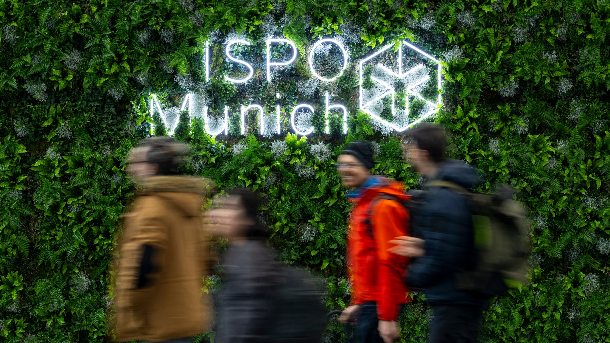 Besucher gehen während der Sportartikelmesse ISPO in der Messe München am Logo "ISPO Munich" vorbei. 