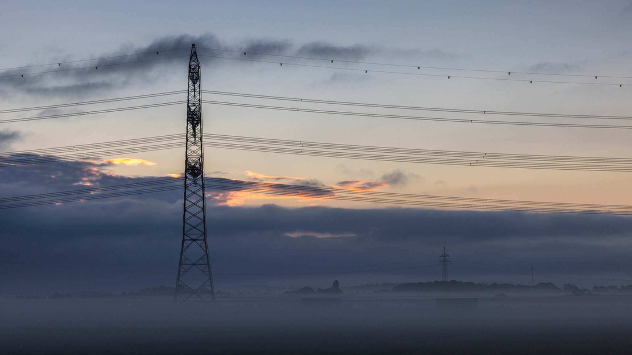 Ein Strommast ist auf einem Feld vom Morgennebel umgeben.