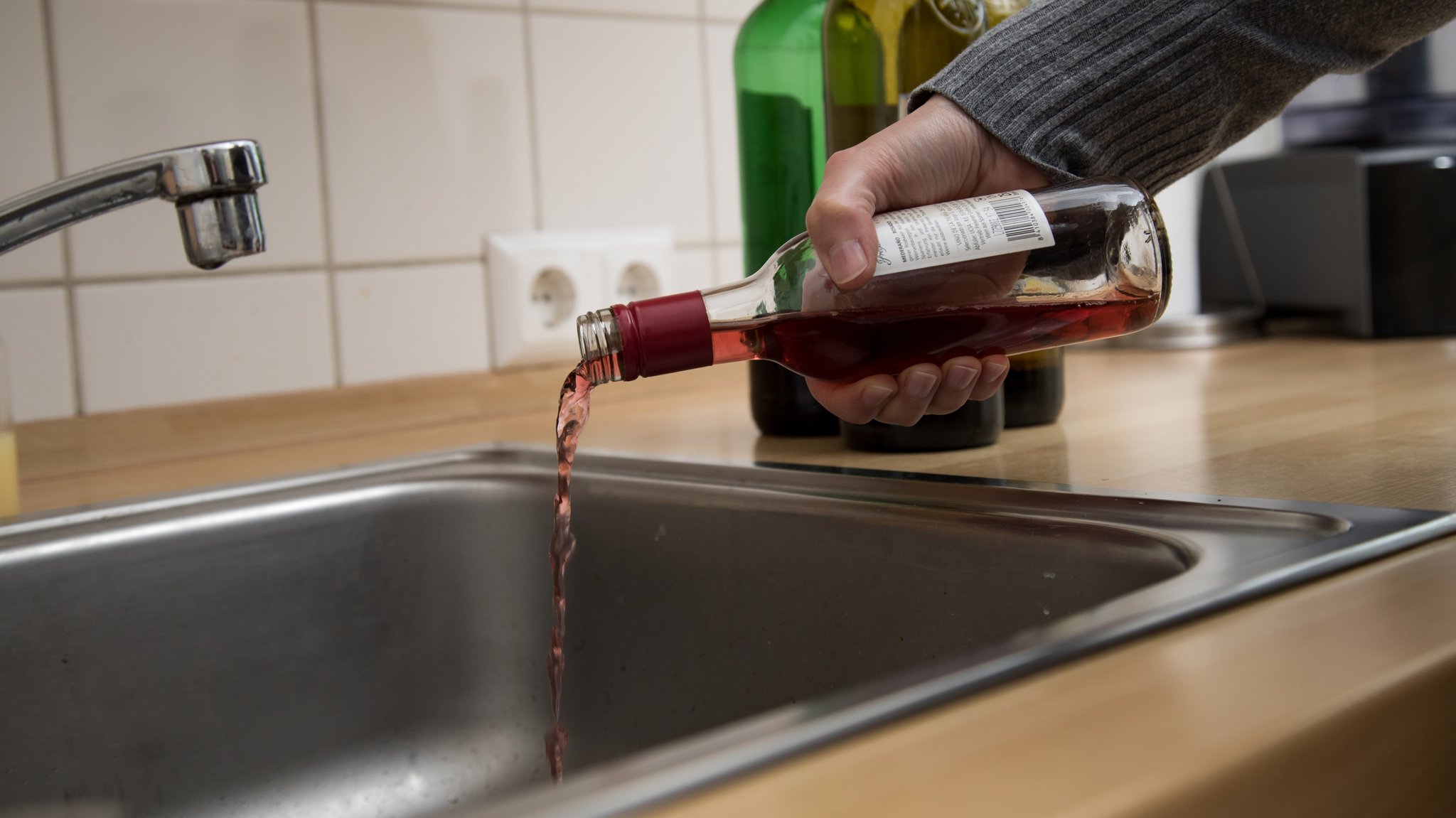 Eine Männerhand entleert eine Flasche Rotwein in den Ausguss.