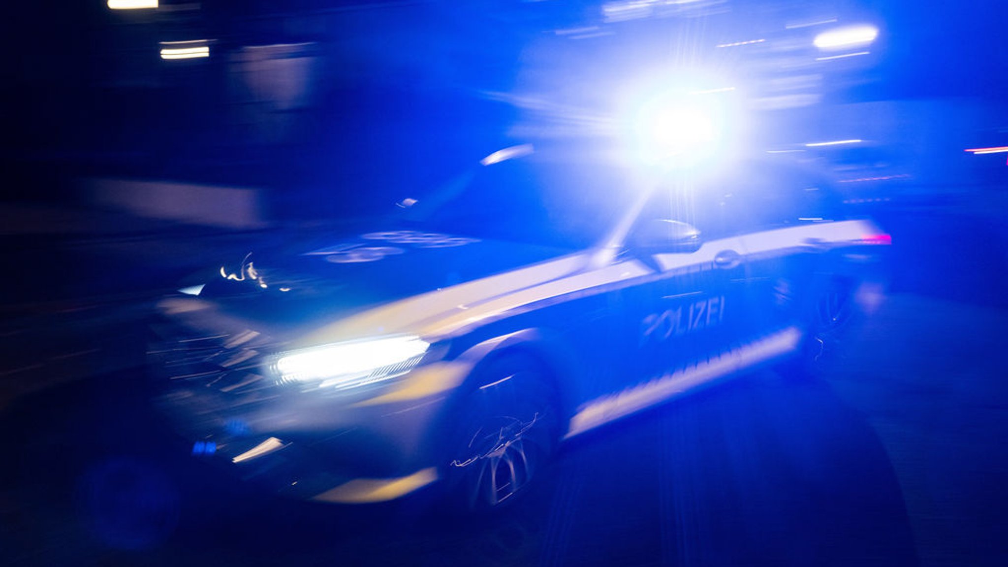 Ein Polizeifahrzeug fährt mit Blaulicht an einem Gebäude vorbei.