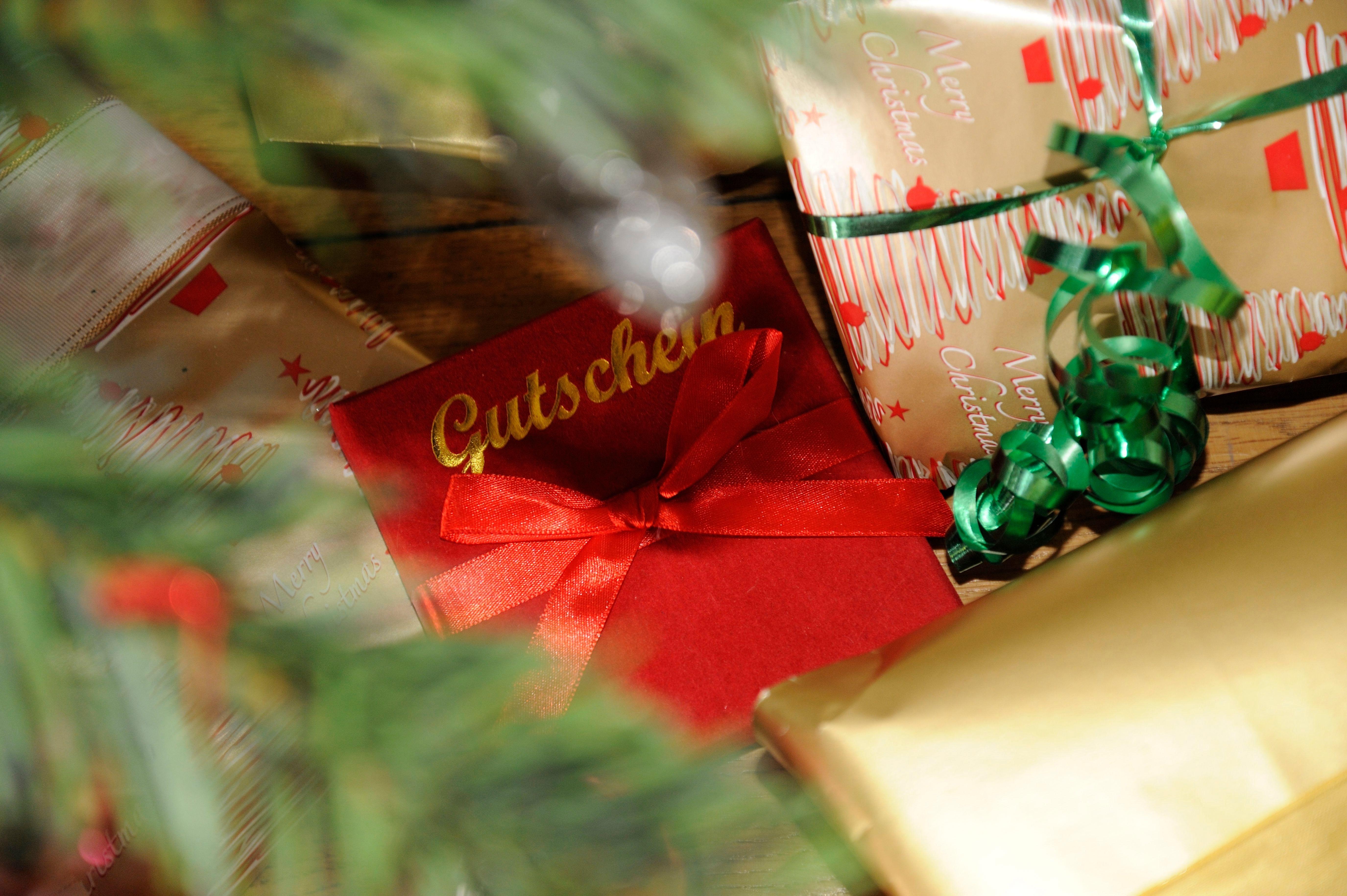 Eine Gutscheinkarte im roten Umschlag mit goldener Schrift neben einem Päckchen mit grüner Kräuselschleife