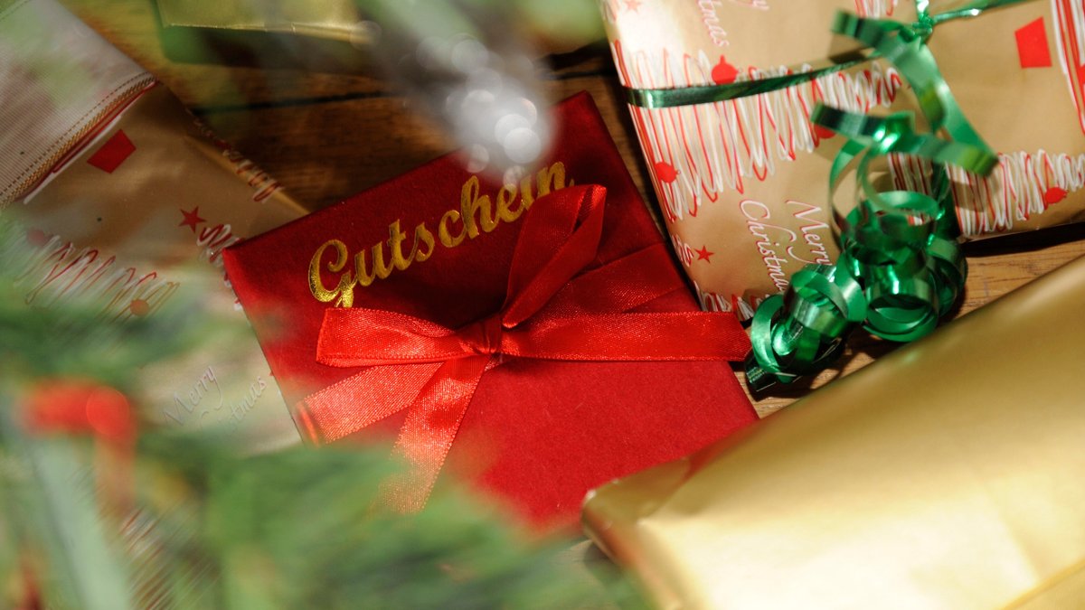 Eine Gutscheinkarte im roten Umschlag mit goldener Schrift neben einem Päckchen mit grüner Kräuselschleife