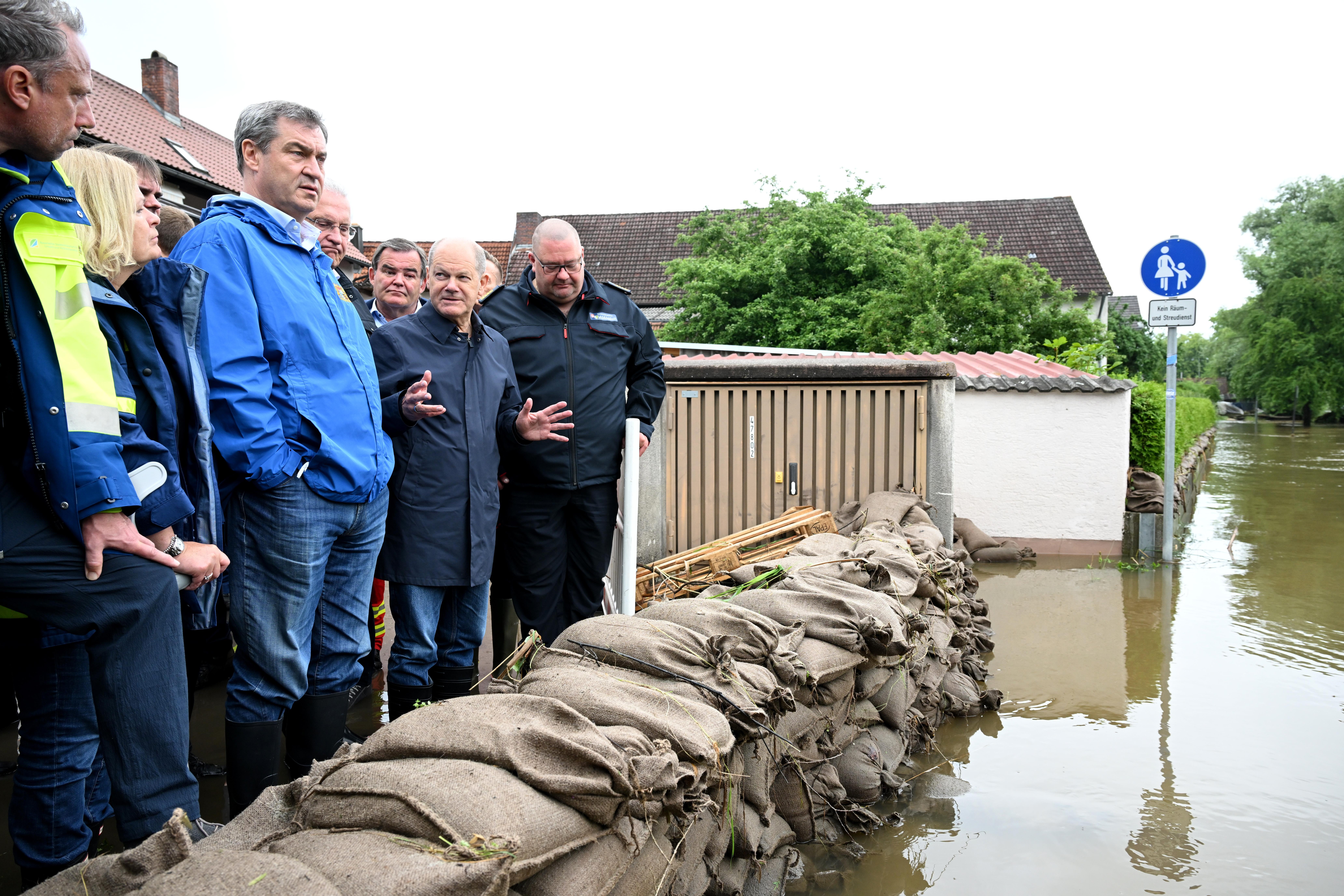 Reichertshofen, 03.06.24: Bundeskanzler Scholz und Bayerns Ministerpräsident Söder (beide mittig im Bild) hinter einer Barriere aus Sandsäcken.