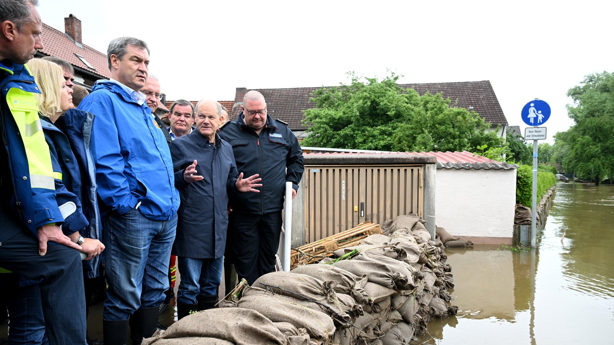 Reichertshofen, 03.06.24: Bundeskanzler Scholz und Bayerns Ministerpräsident Söder (beide mittig im Bild) hinter einer Barriere aus Sandsäcken.