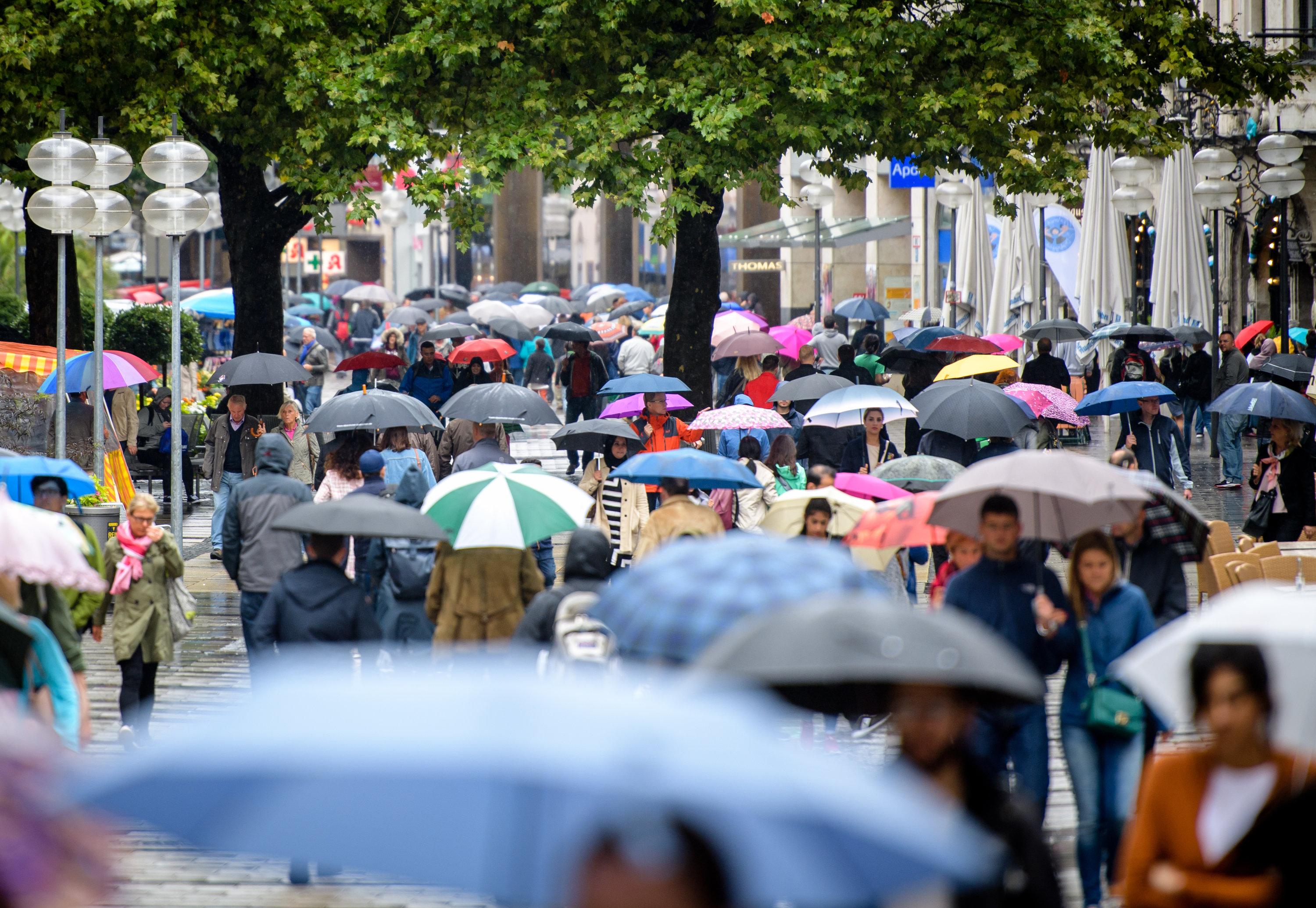 Menschen mit Regenschirmen laufen durch eine Fußgängerzone.
