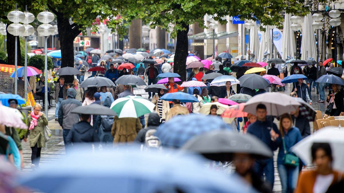 Menschen mit Regenschirmen laufen durch eine Fußgängerzone.