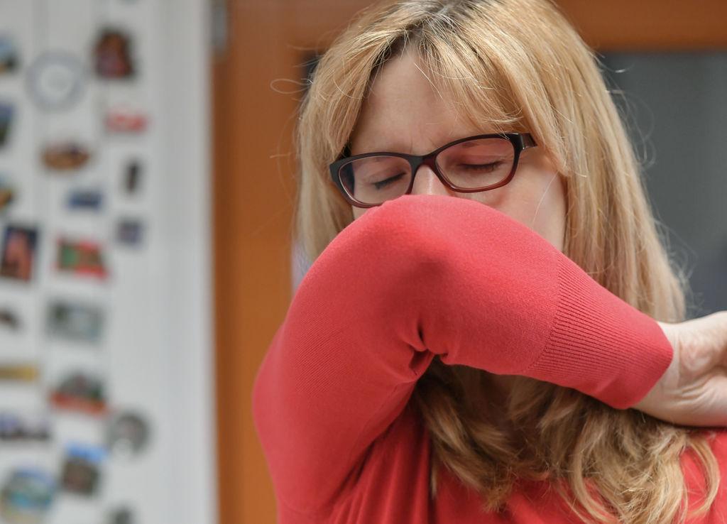 Eine Frau hustet in ihre Armbeuge (gestelltes Foto). 