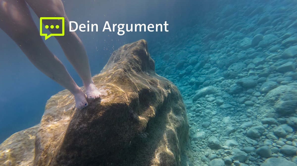 Unter Wasser sind die Beine einer Frau zu sehen, die auf einem Felsen stehen. 