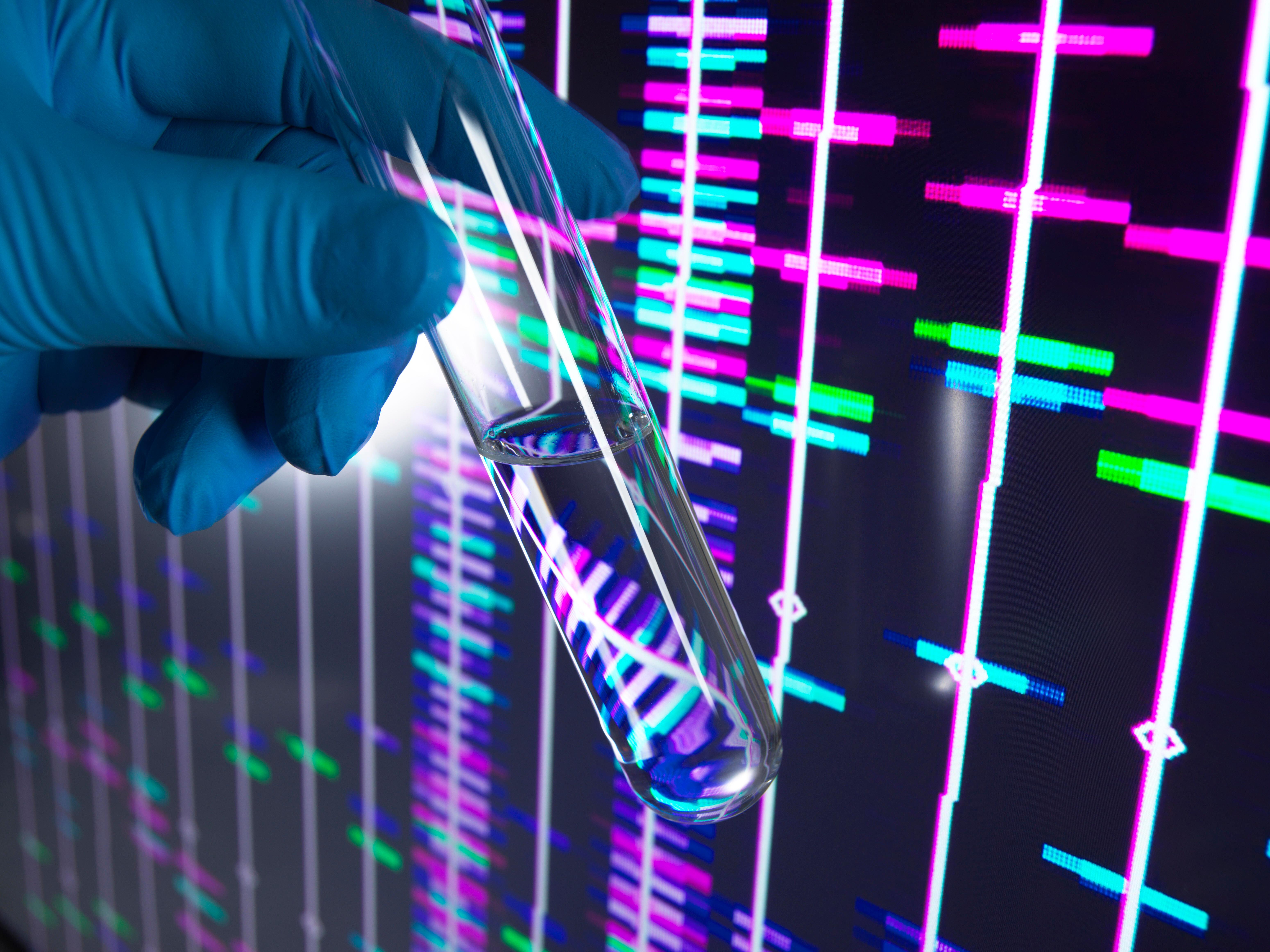 Eine Hand hält ein Reagenzglas vor einen Bildschirm