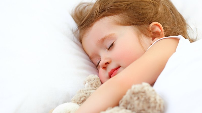 Ein Mädchen schläft mit seinem Kuscheltier im Bett.