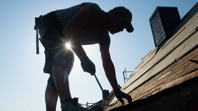 Ein Dachdecker steht auf dem Dach und arbeitet, hinter ihm strahlt die Sonne. | Bild: dpa/pa/Klaus-Dietmar Gabbert Ein Dachdecker steht auf dem Dach und arbeitet, hinter ihm strahlt die Sonne.