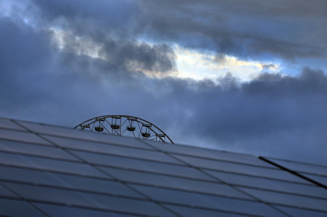 Das Riesenrad des Freizeitparks Allgäu Skyline Park, steht am frühen Morgen vor wolkenüberzogenen Himmel hinter den Paneelen einer Solaranlage.