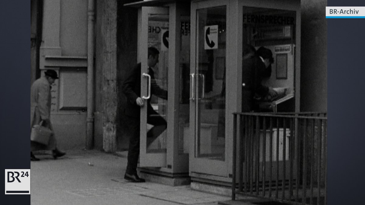 Zwei Telefonzellen nebeneinander, bei der linken ist die Türe geöffnet, Mann betritt Telefonzelle