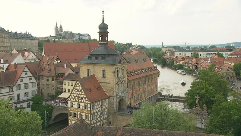Das historische Rathaus mit einem Fachwerkgebäude an der Unteren Brücke von oben betrachtet, im Hintergrund zwei Schiffe auf der Regnitz.