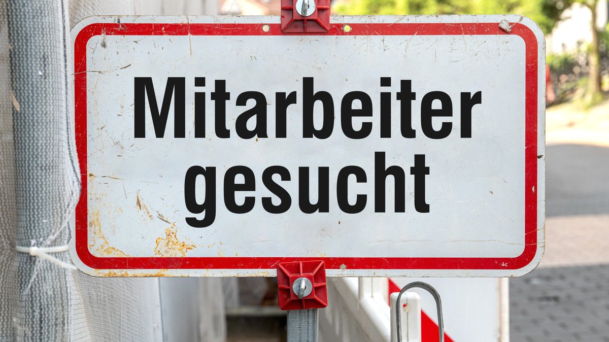 Ein weißes Schild mit Aufschrift "Mitarbeiter gesucht". Foto mit Composing als Symbolbild für den Fachkräftemangel in Deutschland.