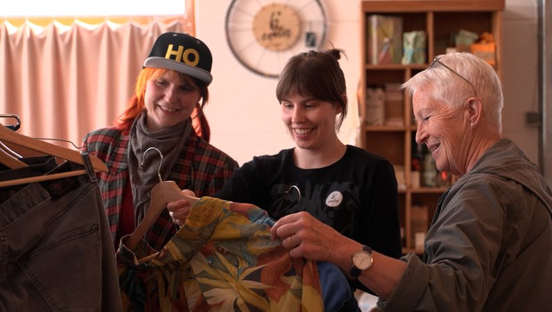 Drei Frauen sehen sich Kleidungsstücke an. | Bild: BR Drei Frauen sehen sich Kleidungsstücke an.