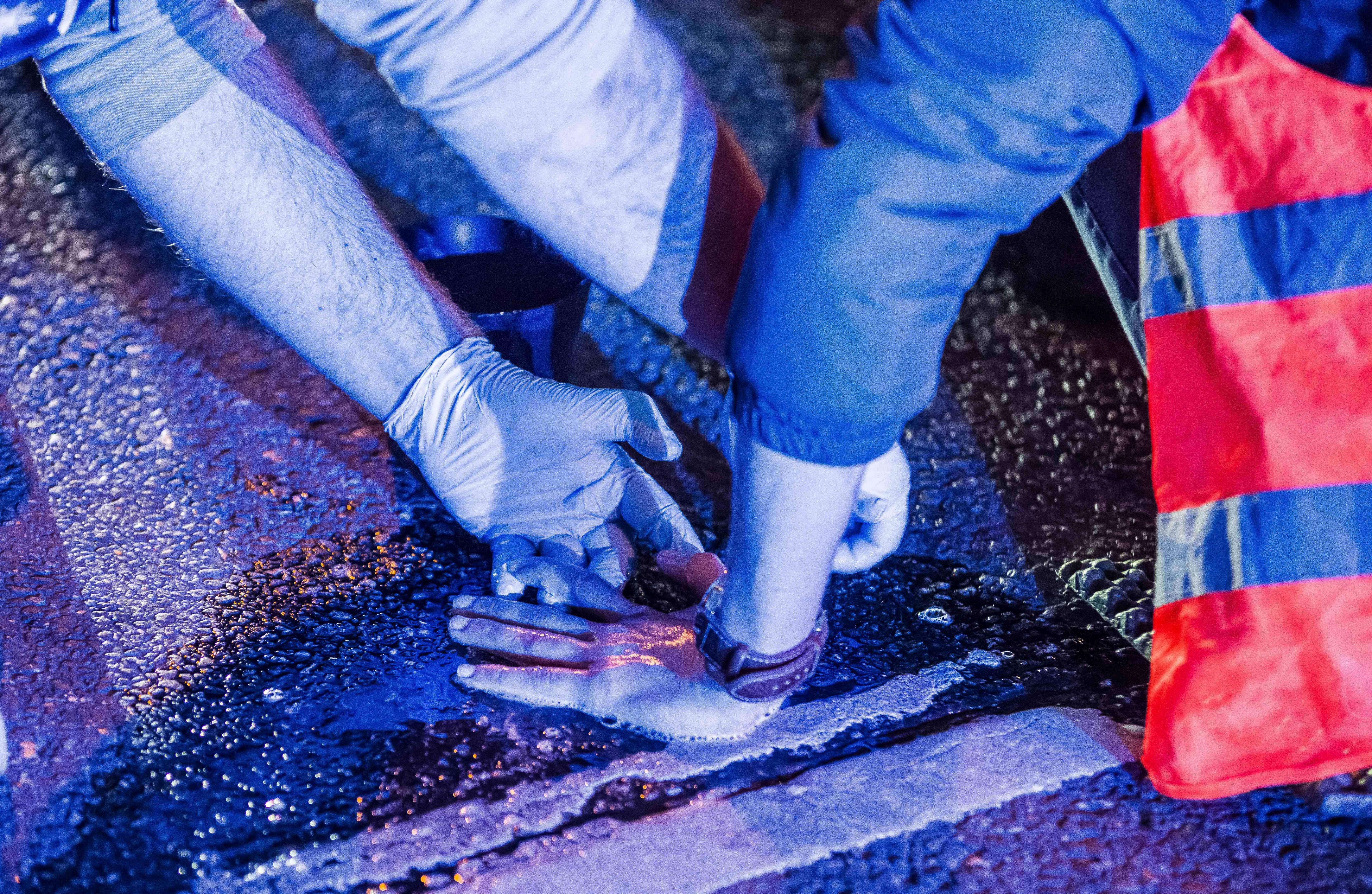 Ein Polizist versucht, die festgeklebte Hand eines Mannes von der Straße zu entfernen.
