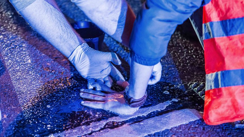 Ein Polizist versucht, die festgeklebte Hand eines Mannes von der Straße zu entfernen. | Bild: pa/ZUMAPRESS.com/Sachelle Babbar Ein Polizist versucht, die festgeklebte Hand eines Mannes von der Straße zu entfernen.