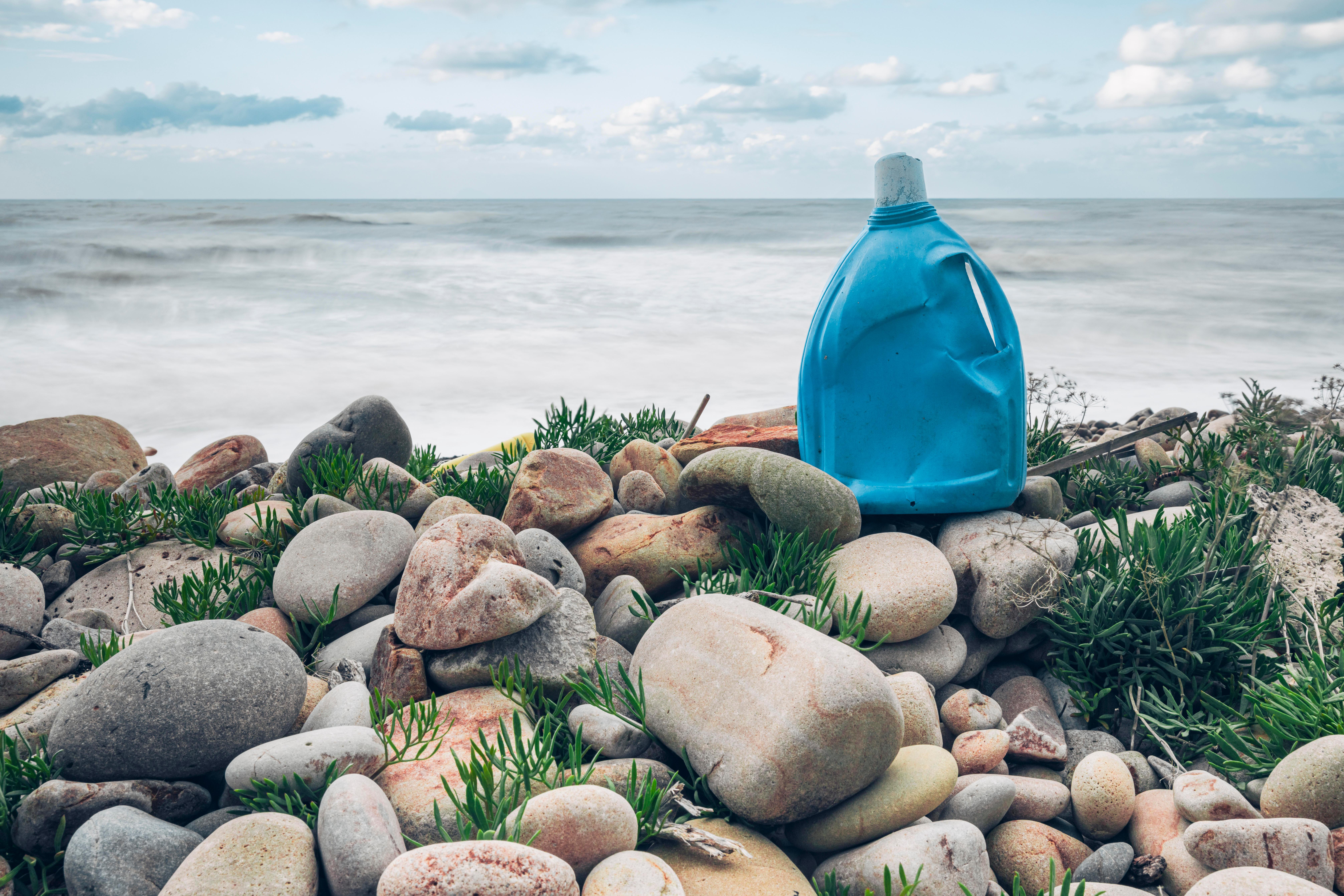 Eine blaue Plastik-Waschmittelflasche vermüllt einen Kiesstrand