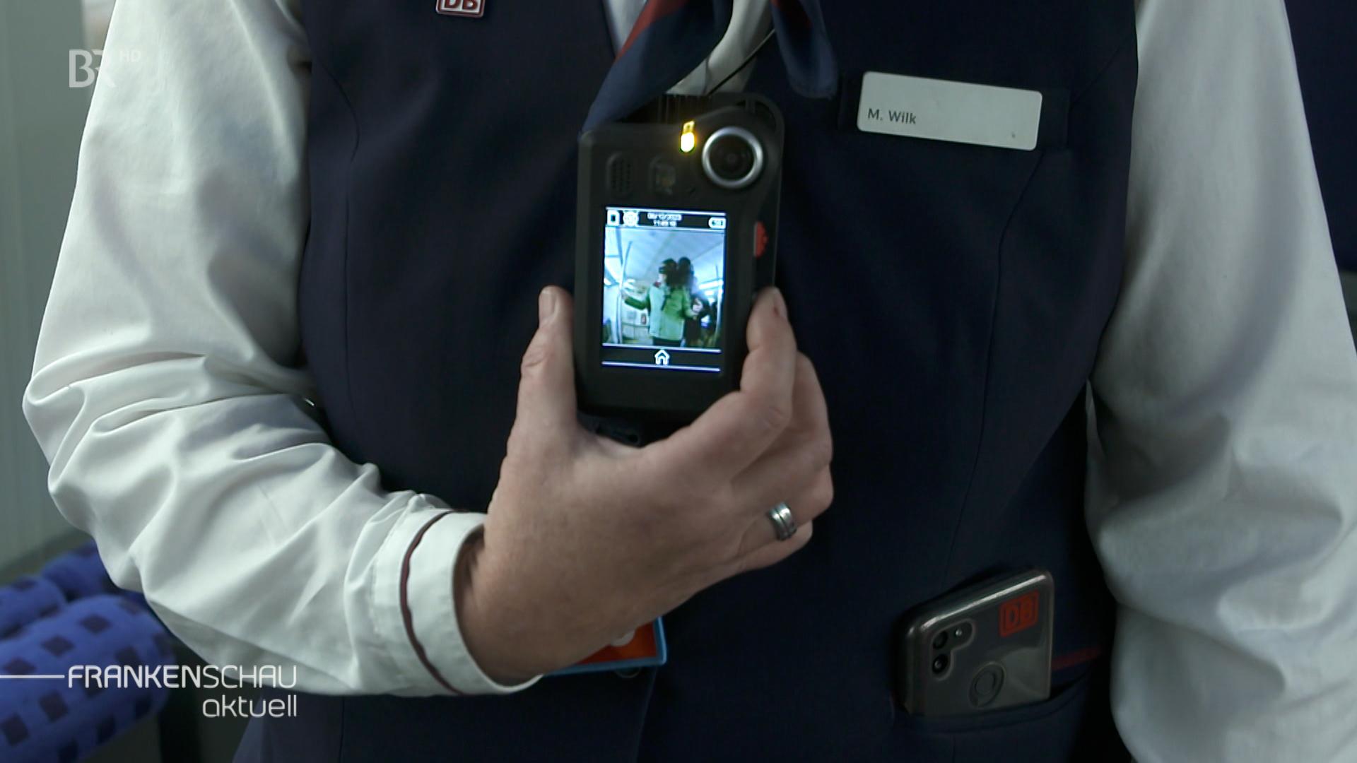 Eine Hand hält eine Bodycam, die am Oberkörper hängt. 