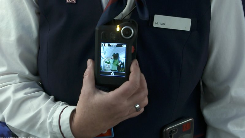 Eine Hand hält eine Bodycam, die am Oberkörper hängt. 