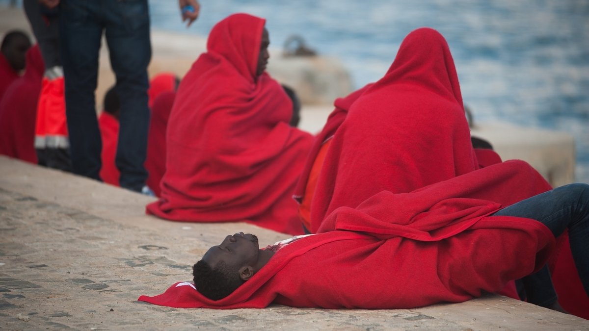 Flüchtlinge nach ihrer Rettung aus dem Mittelmeer in Decken gehüllt am Ufer