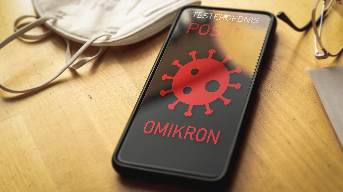 Smartphone liegt auf einem Tisch neben einer FFP 2 Maske mit der Warnung auf dem Display: Testergebnis Positiv Omikron
