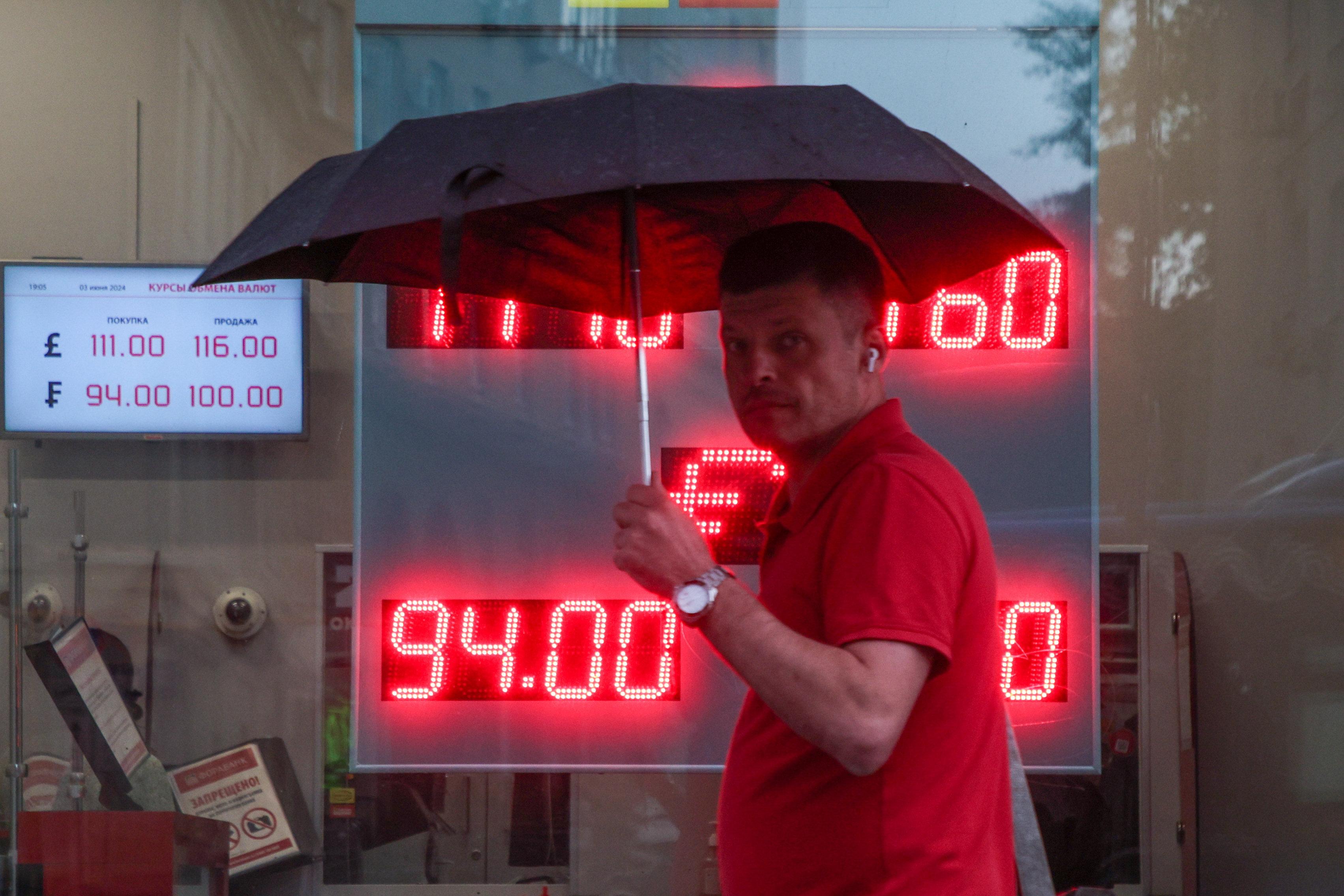 Mann mit Schirm geht vor Anzeigentafel vorbei