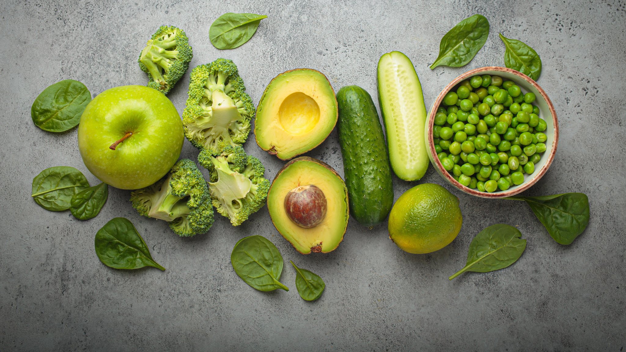 Äpfel, Brokkoli, Avocados, Gurken und grüne Erbsen, appetitlich angerichtet auf einem Tisch