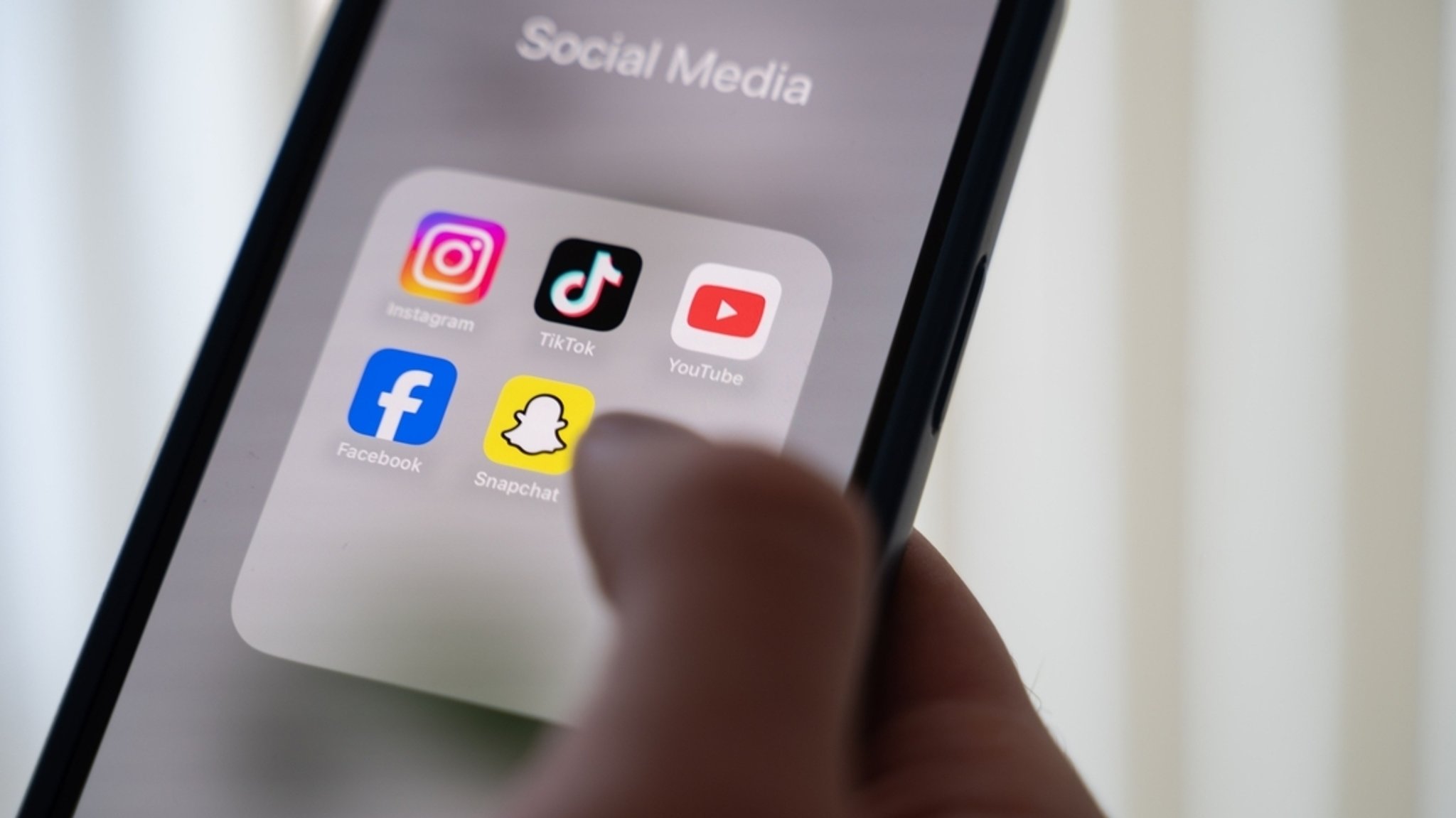 (Symbolbild) Eine Frau hält ein Smartphone, auf dessen Display verschiedene Social Media Apps angezeigt werden.