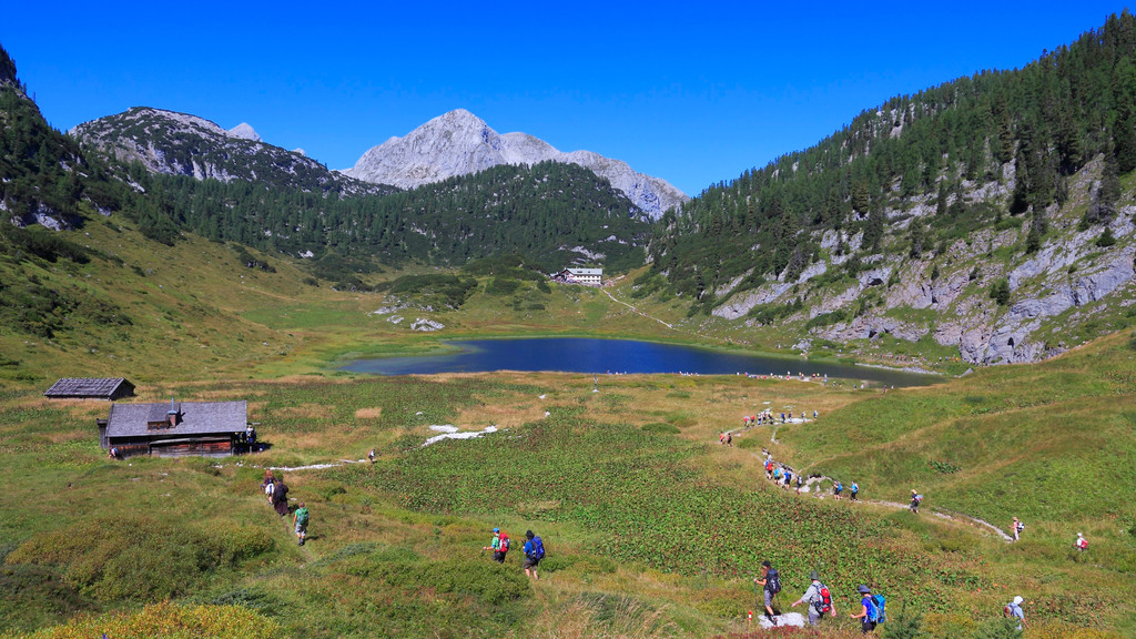 Der Funtensee im Nationalpark Berchtesgaden und Menschen, die auf den See zulaufen; im Hintergrund die Bergkulisse des Nationalparks Berchtesgaden.