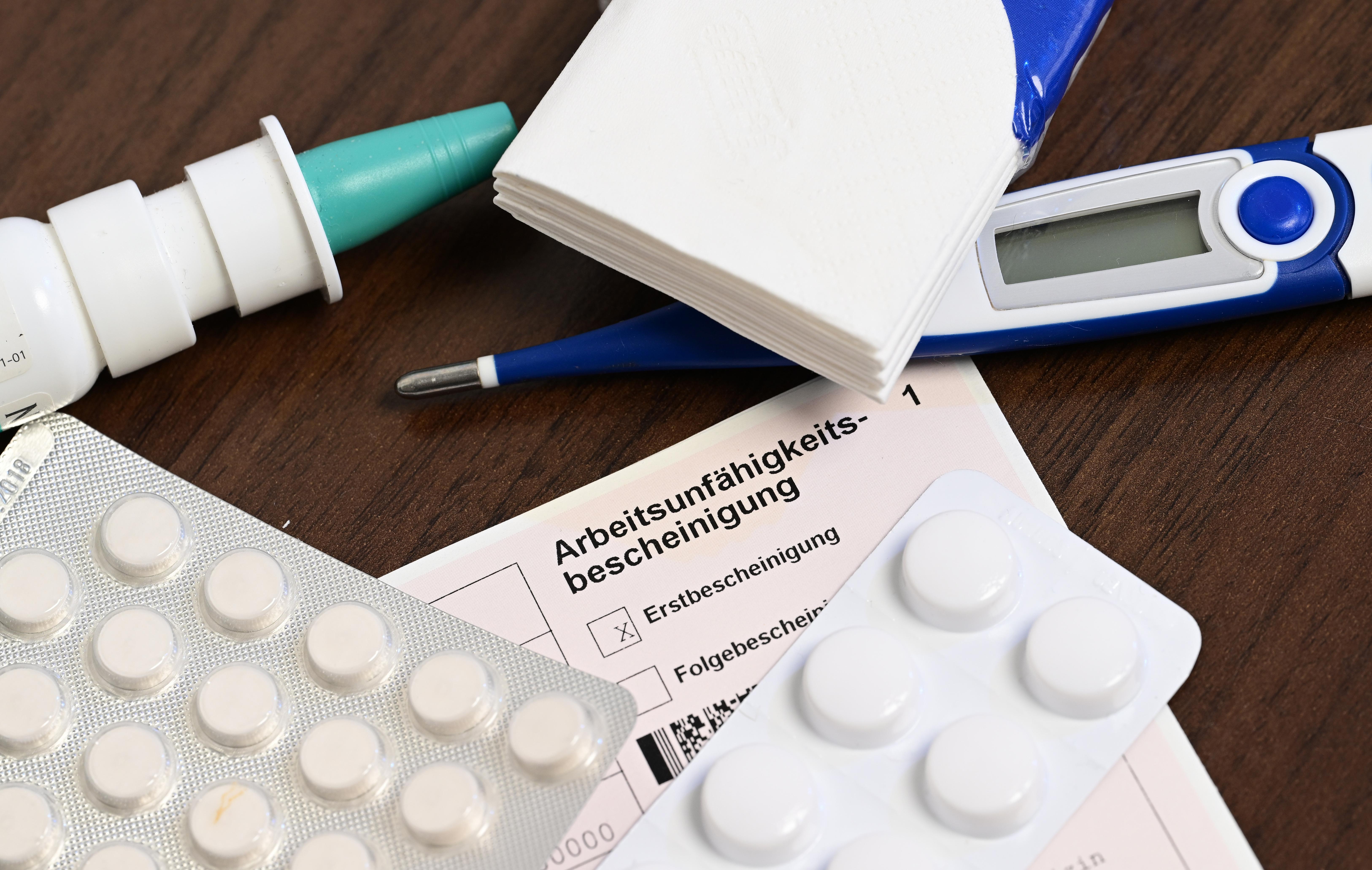 Ein Fieberthermometer, Medikamente und eine ärztliche Arbeitsunfähigkeitsbescheinigung