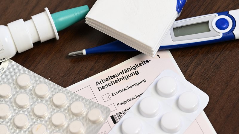 Ein Fieberthermometer, Medikamente und eine ärztliche Arbeitsunfähigkeitsbescheinigung | Bild: picture alliance/dpa | Bernd Weißbrod Ein Fieberthermometer, Medikamente und eine ärztliche Arbeitsunfähigkeitsbescheinigung